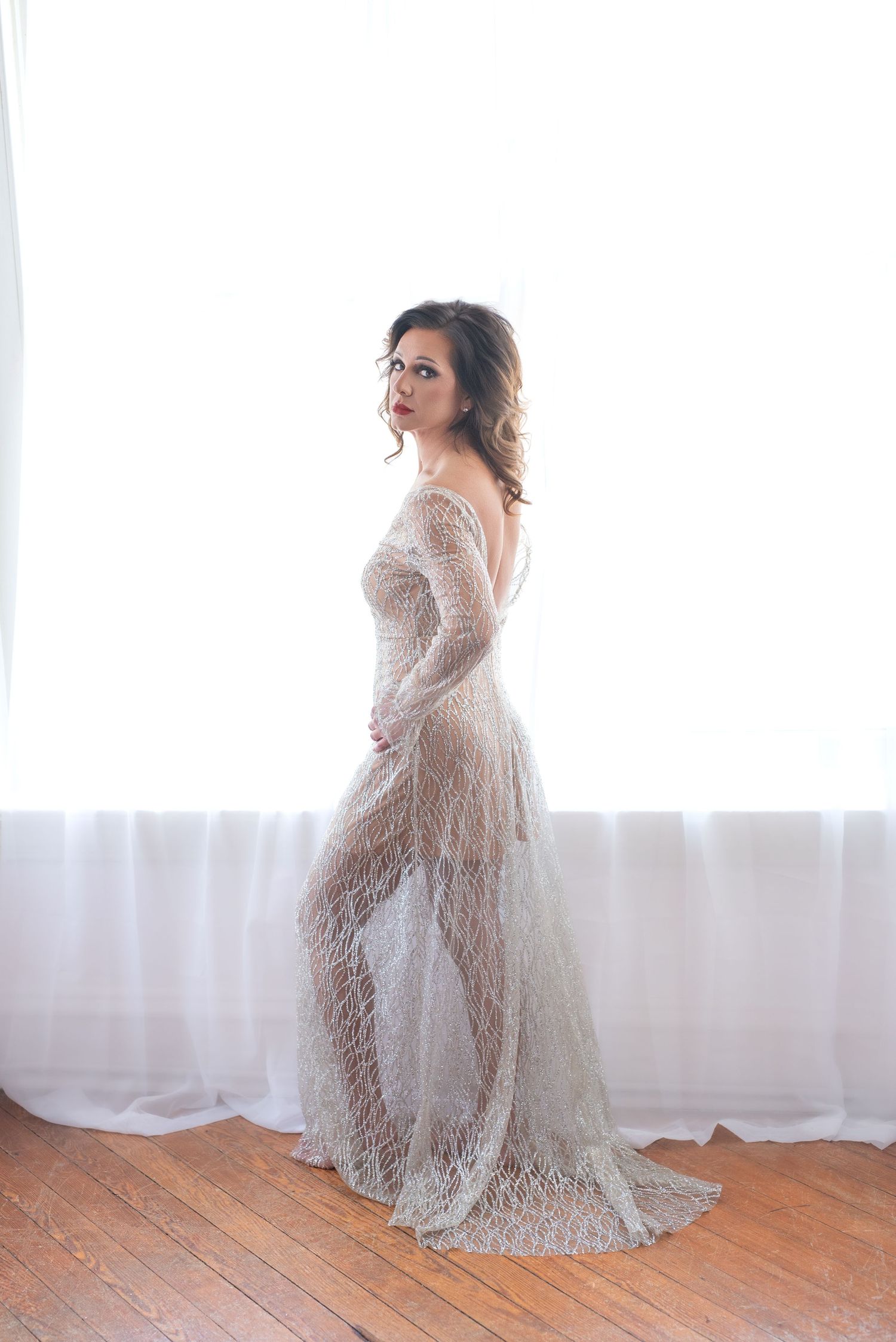 Woman in her 50's posing in a glittery bodysuit stands beside white column in dramatic boudoir photoshoot in cape girardeau, missouri