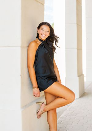 Athletic poses in a black halter top against white architectural columns.