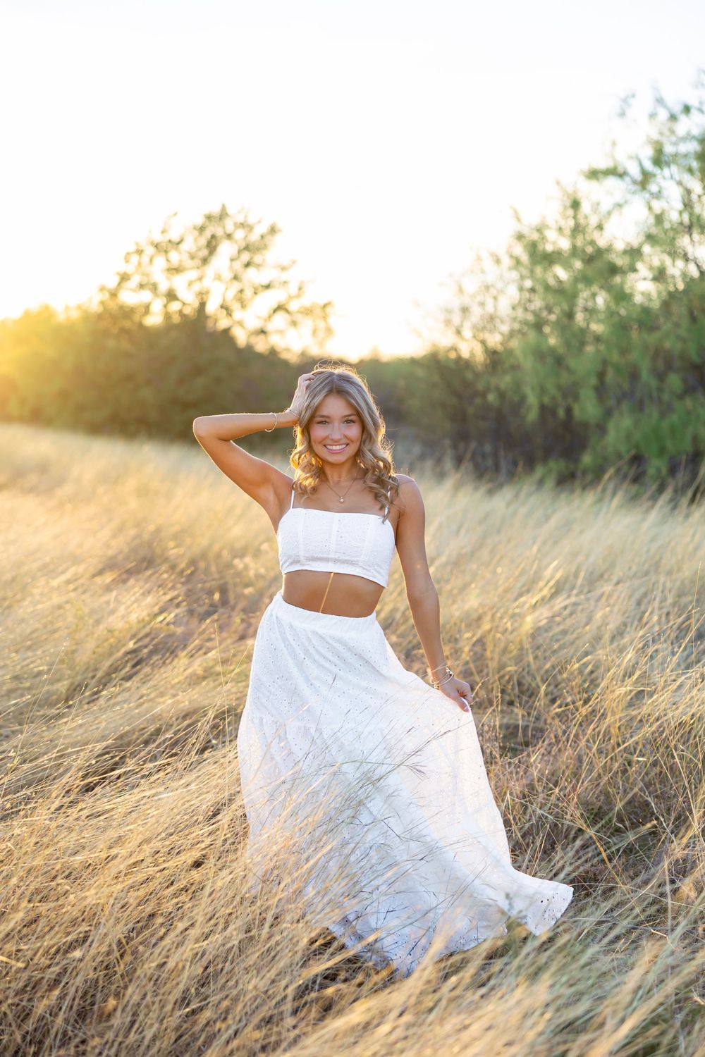 Model in white two-piece outfit poses in golden field during sunset.