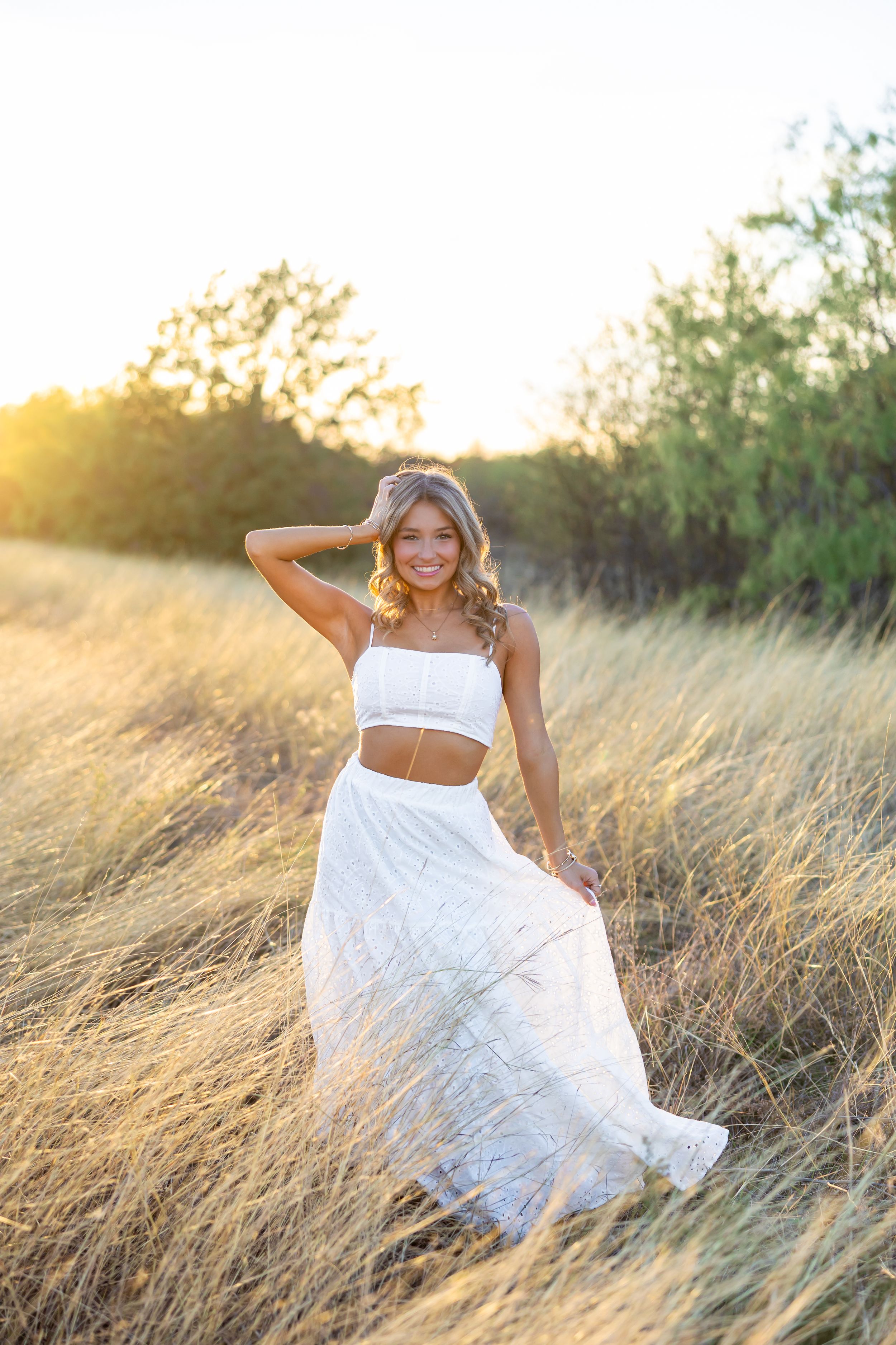 Model in white two-piece outfit poses in golden field during sunset.