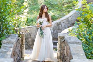 Woman in flowing white dress stands among garden greenery.