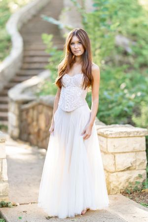Woman in white lace dress poses along garden stone pathway.