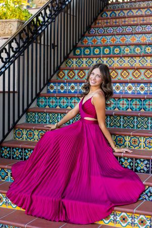 A person poses in a magenta dress on colorful tiled stairs with decorative railings.