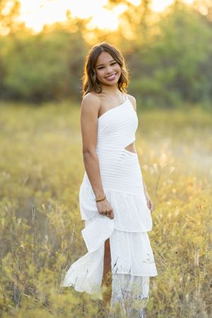 Sunset portrait session in a field with someone wearing a white ruffled dress.