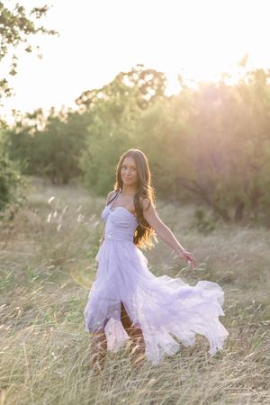 A flowing white dress twirls gracefully in a sunlit field of tall grass during golden hour.