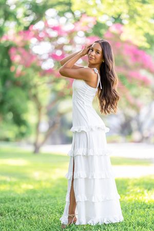 White tiered dress flows elegantly against a vibrant garden backdrop with pink flowers.