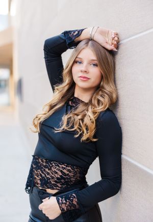 Portrait series against white wall wearing black lace top with styled wavy hair.