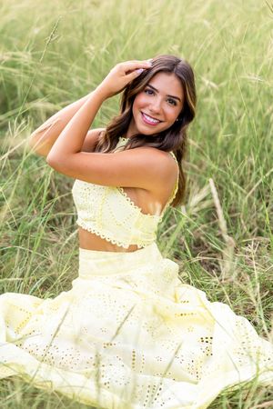 A person in a flowing white eyelet dress poses gracefully in a sunlit meadow of tall grass.