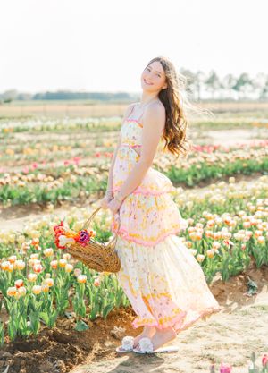 A floral sundress-clad figure poses gracefully in a blooming tulip field at sunset.