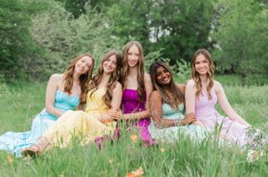 A group relaxes on blankets in a lush green field wearing pastel spring dresses.