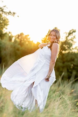 Woman in flowing white dress twirls gracefully in a sunlit field during golden hour.