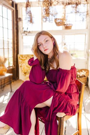 Interior photoshoot featuring burgundy dress poses by sunlit windows with dried flowers.