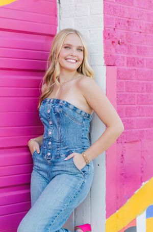 Lifestyle portraits against pink wall wearing denim overalls in urban setting.