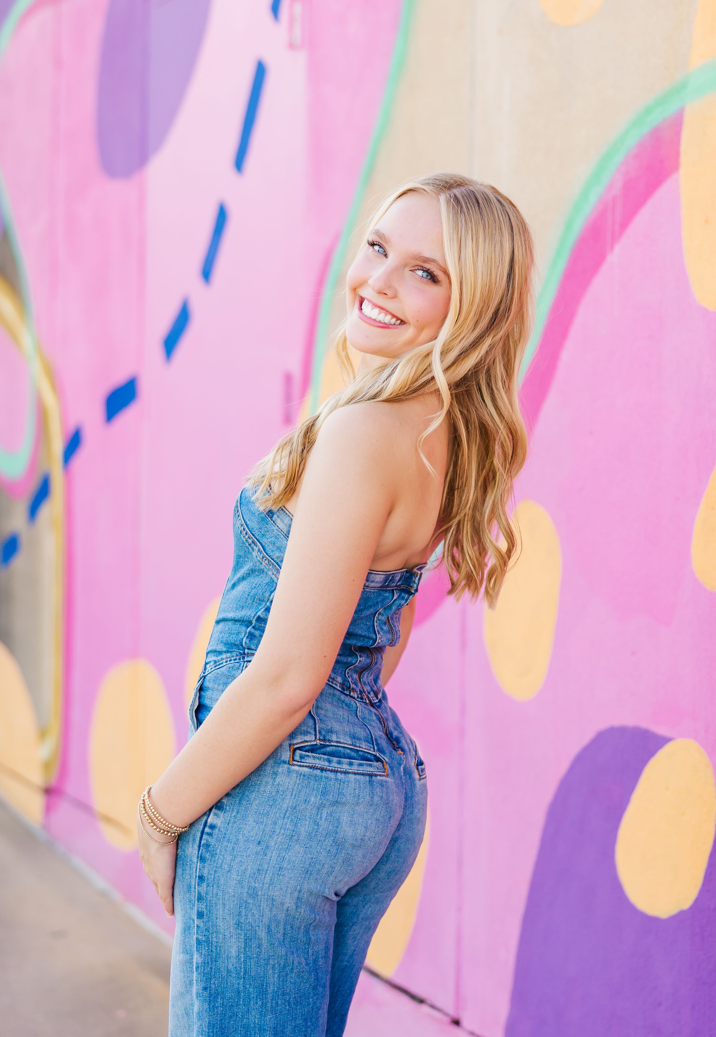 Fashion portraits against colorful painted wall wearing denim overalls and natural styling.