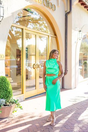 Stylish poses in a mint green dress against Mediterranean-style architecture.