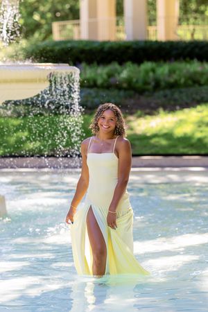 Playful water fountain photoshoot with a flowing yellow dress on a sunny day.