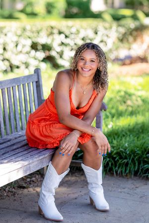 Fashion portrait with white boots and orange dress on a garden bench.