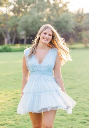 Person wearing light blue ruffled top poses in sunny outdoor setting.
