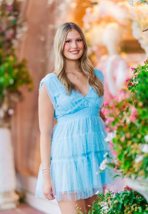 Portrait in light blue ruffle top among blooming flowers during golden hour.