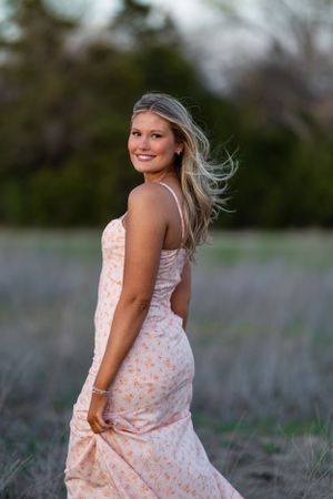 Person in floral dress poses gracefully in field during golden hour.