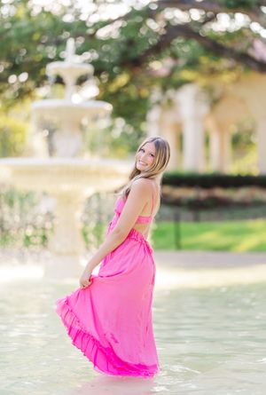 Person in bright pink dress twirling in water during golden hour photoshoot.