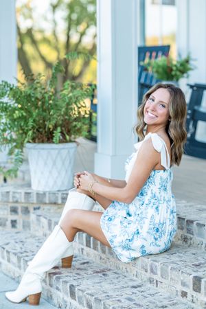 Someone in a blue and white patterned dress poses on brick steps near white planters.