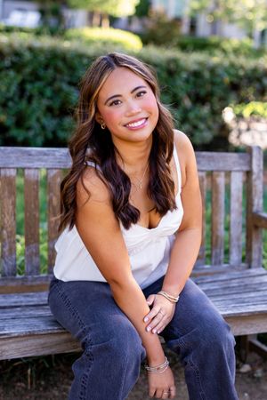 Casual portrait of person sitting on wooden bench in garden setting.