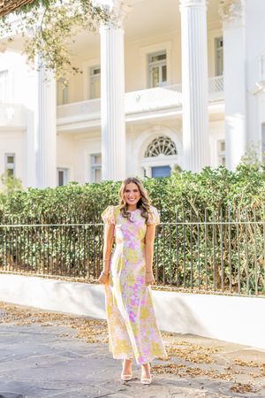 Woman in floral print dress standing in front of white columned building on sunny day.