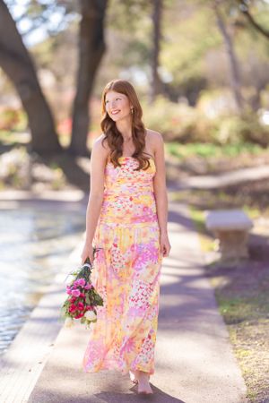 Floral print dress photoshoot on a sunny garden path with red flowers.