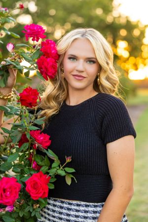 A portrait against vibrant red roses and sunset lighting featuring a black ribbed top and patterned skirt.