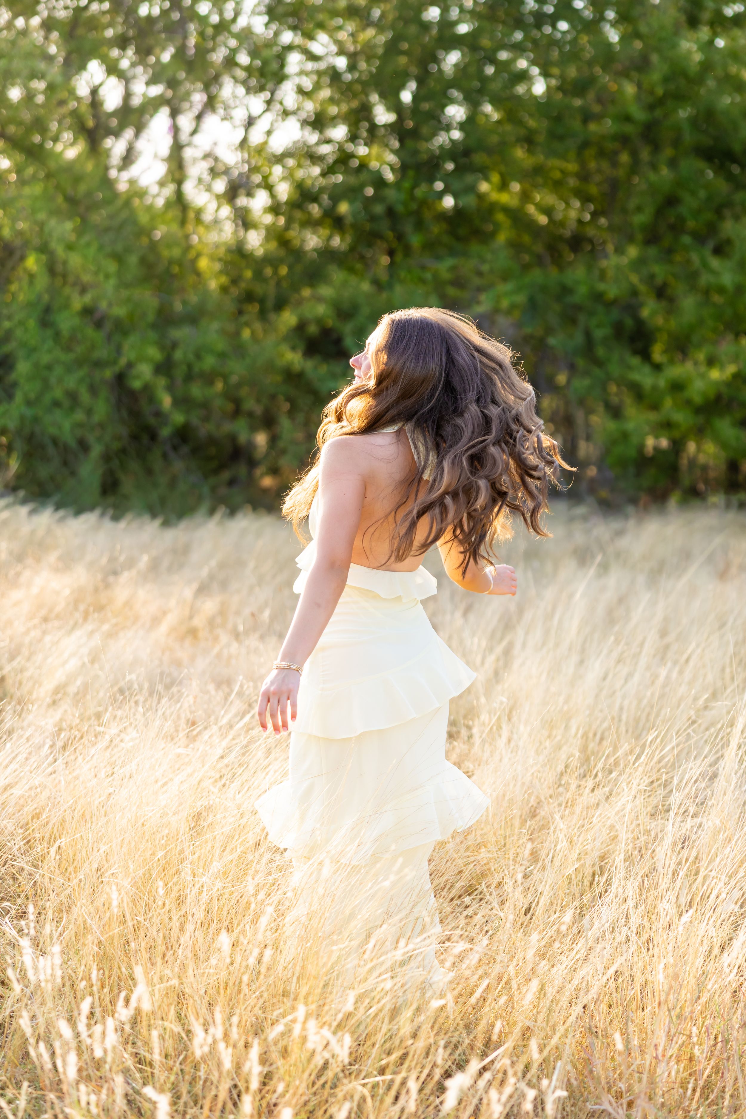 Woman in white strapless dress twirling in golden field with long flowing hair, bathed in warm sunset light.