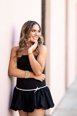 Woman in black dress poses against light colored wall in a series of elegant fashion portraits.