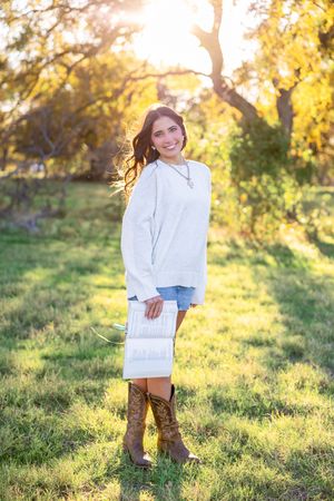 Person wearing white sweater and boots poses in autumn park setting.