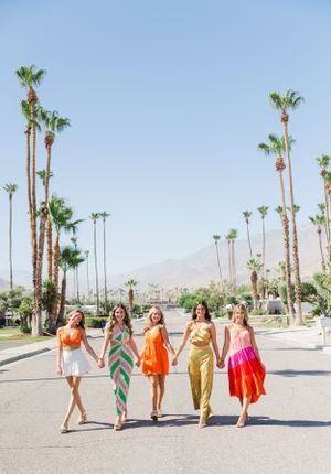 Friends in colorful summer dresses walking together among palm trees.