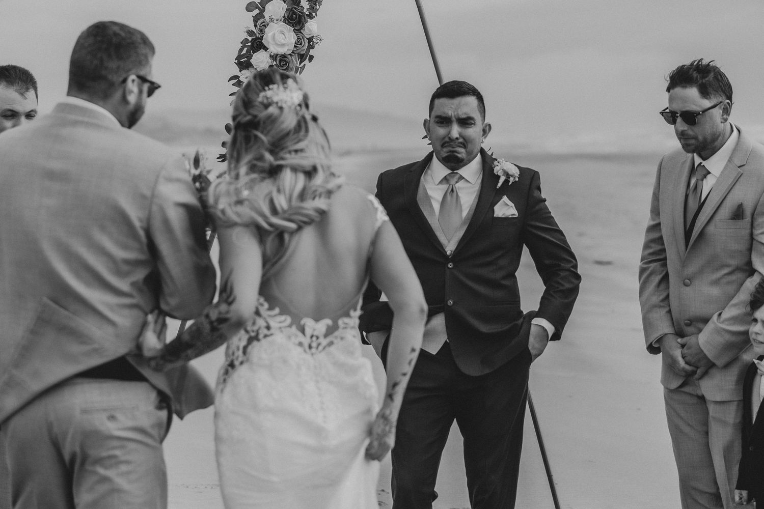 Black and white photograph of a group at a wedding ceremony with the bride in a white gown and groom in a dark suit.