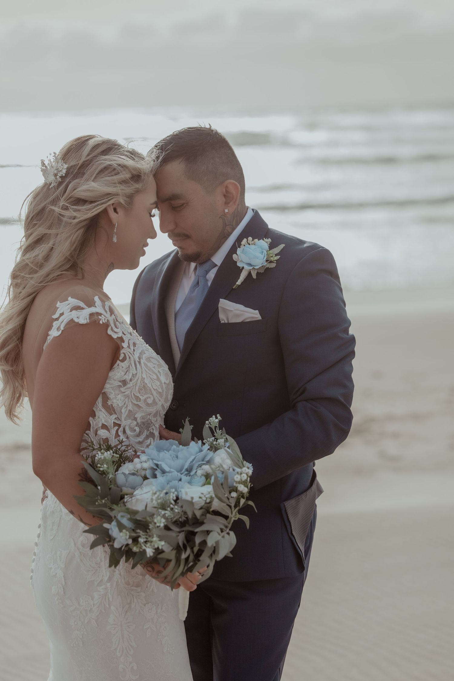 Newlywed couple sharing romantic moments on a misty beach with soft waves in the background.