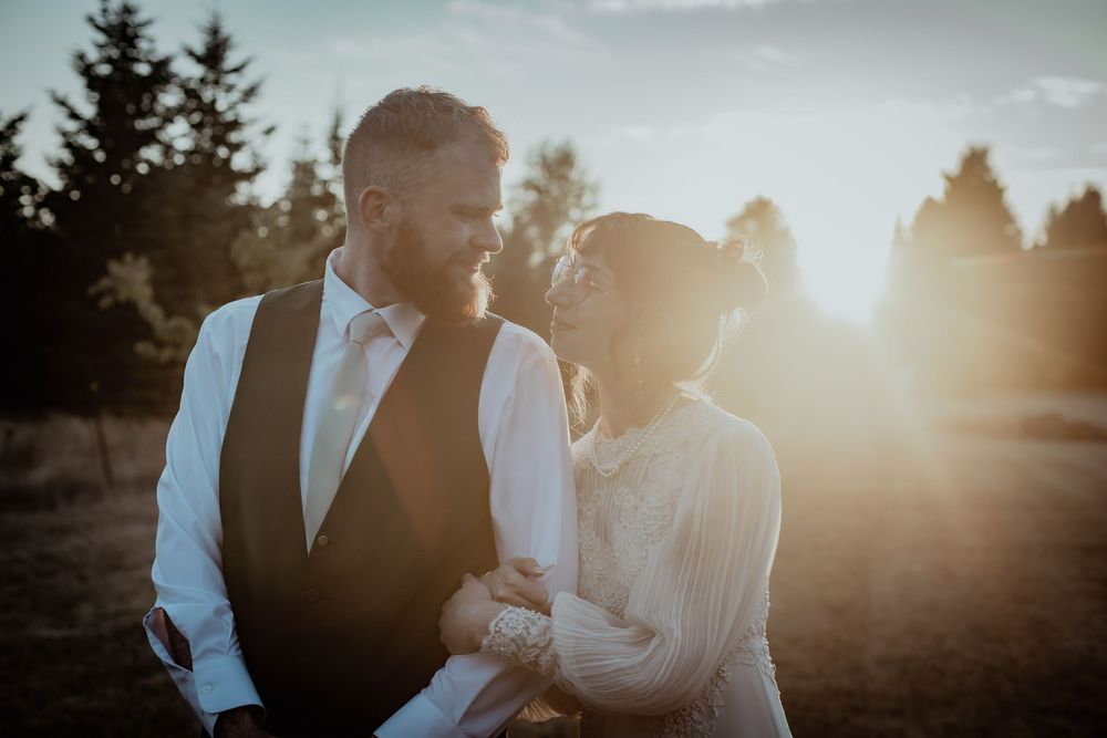 A couple shares a romantic moment at sunset with evergreen trees silhouetted in the background.