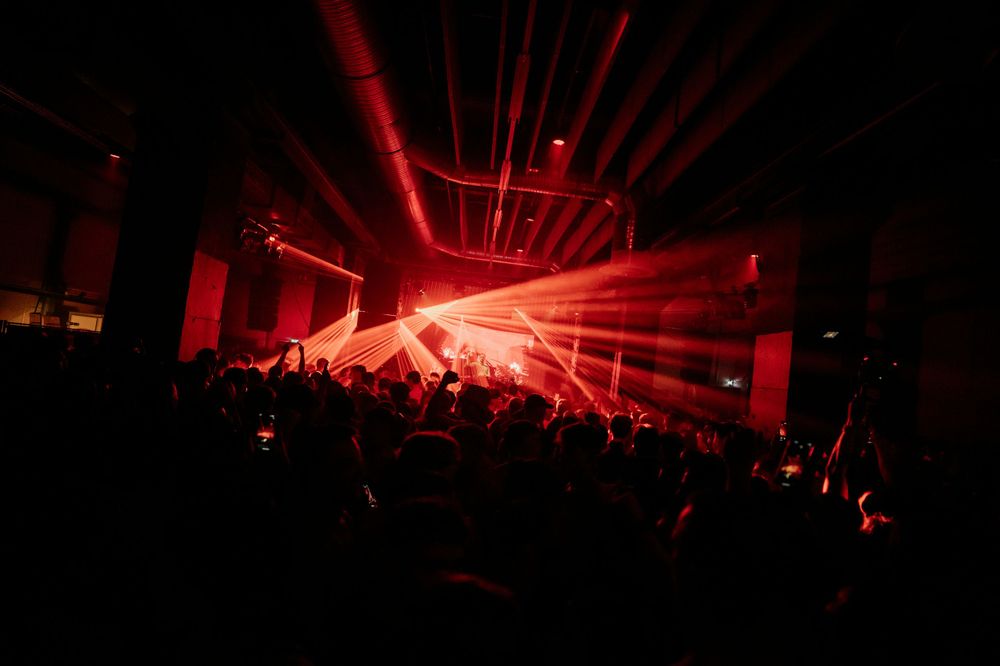 Red laser beams illuminate a packed concert venue during a nighttime performance.