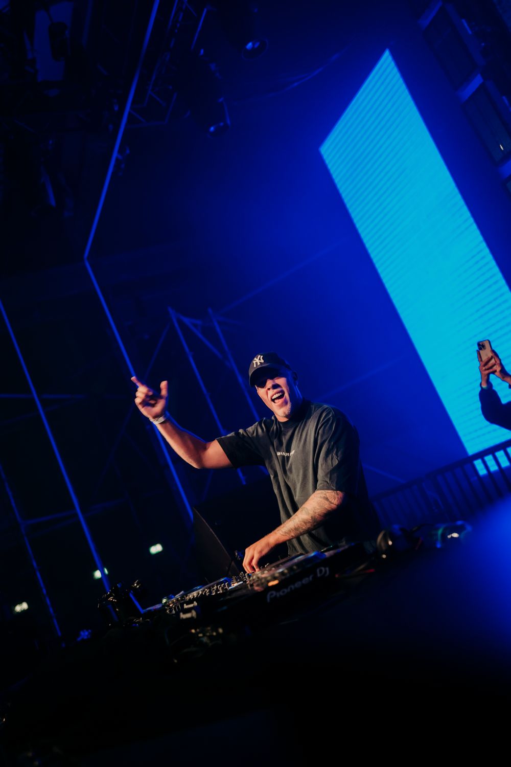 DJ performing on stage with vivid blue lighting and geometric visual backdrop.