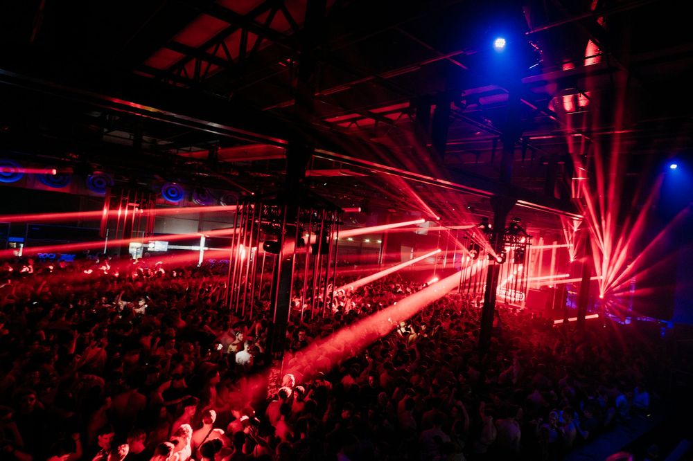 Wide shot of concert venue with dramatic red and blue lighting effects during electronic music show.