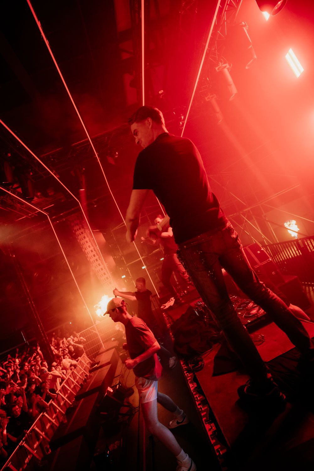Concert performers on stage bathed in intense red lighting during an energetic live performance.