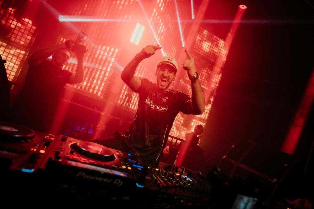 DJ performing at a nightclub with dramatic red lighting and smoke effects creating an energetic atmosphere.