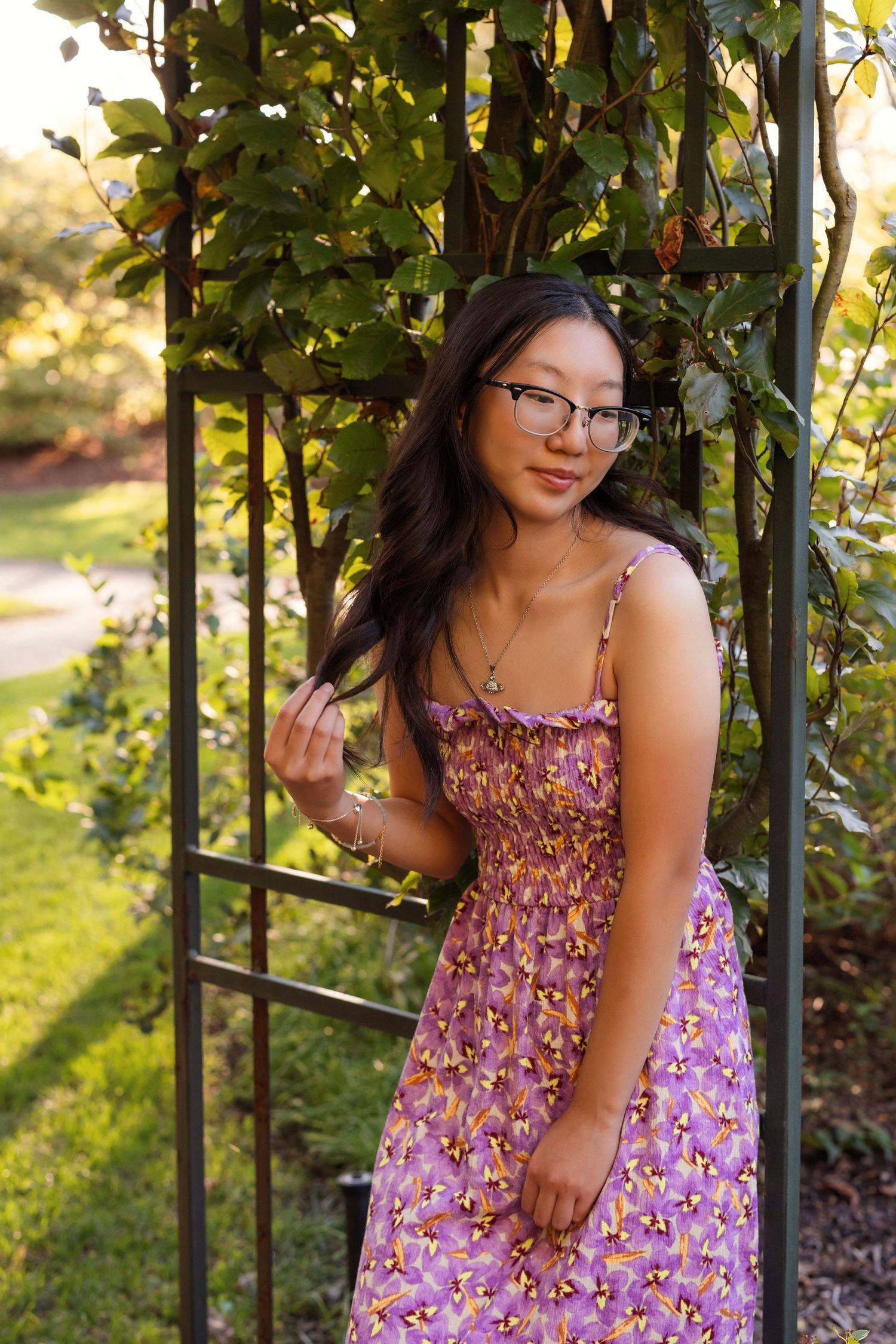 Person in purple floral dress posing by garden trellis at sunset.