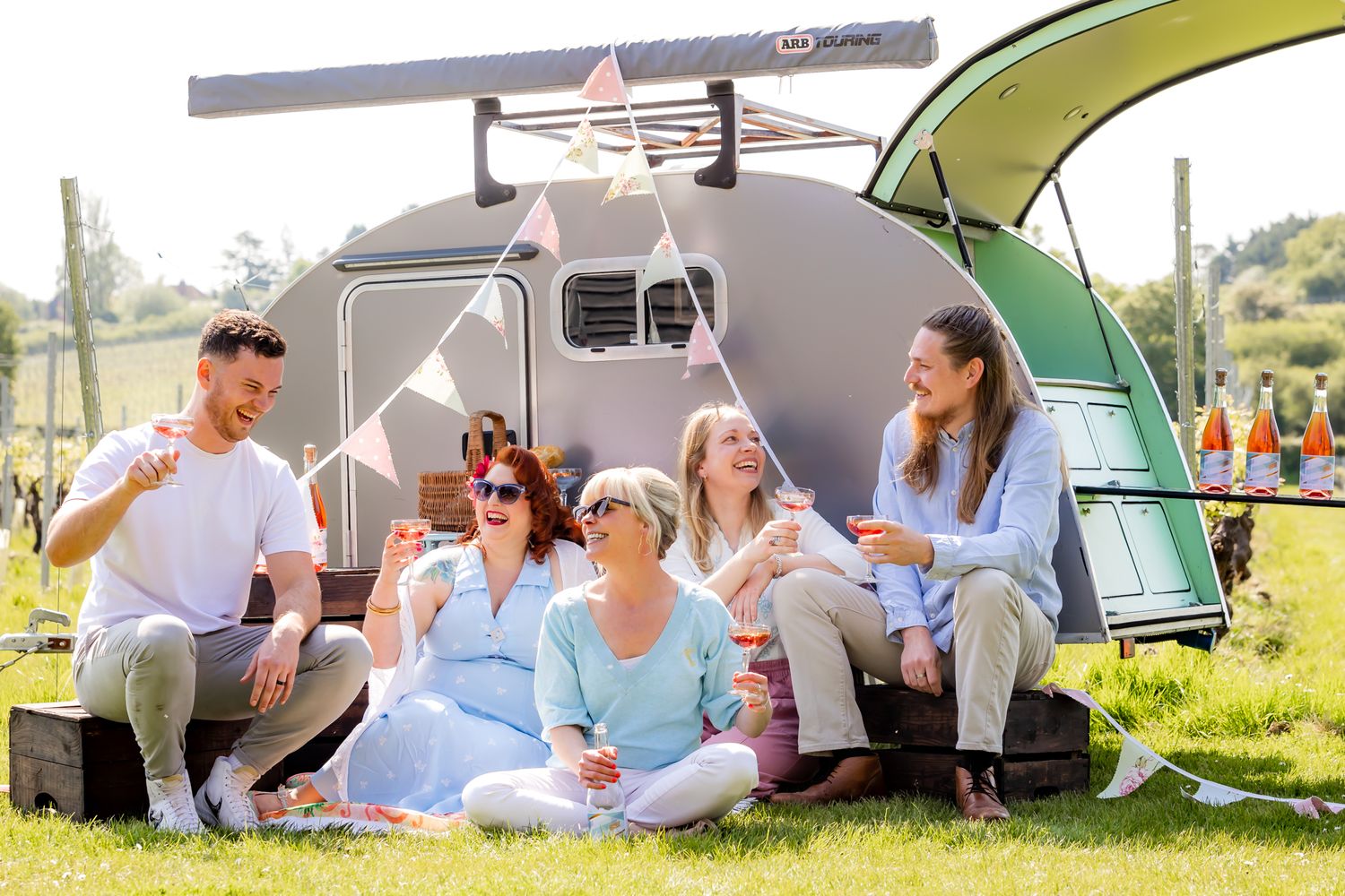 Group enjoying outdoor camping beside vintage trailer and green canopy.