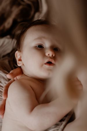 Close-up portret van een baby tijdens een voedingsmoment met een nieuwsgierige uitdrukking tegen een zachte bruine achtergrond.