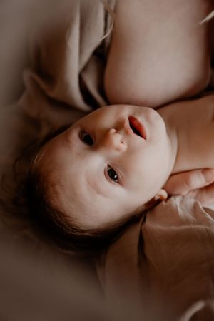Bovenaanzicht van een baby tijdens een voedingsmoment met stralende ogen, liggend op zachte stof in gedempte tinten.