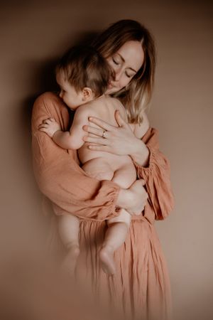 Intiem portret in warme tinten waarop een tedere omhelzing tussen ouder en baby wordt vastgelegd.