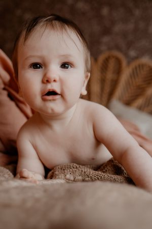Lief close-up portret van een baby op textuur beddengoed, met een gevlochten hoofdbord op de achtergrond.