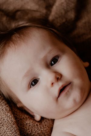 Intiem portret van een baby met stralende ogen, liggend op bruin textuurstof.