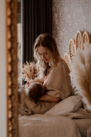 Rustig moment waarop een ouder de baby voedt in een slaapkamer met boho-decor en pampasgras.